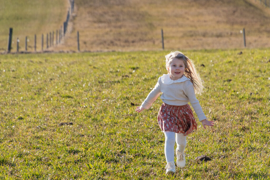Junges Mädchen läuft über die grüne Wiese in der Nahe von Ybbs an der Donau. Im Hintergrund ist ein Zaun zu sehen und die Erde hat einige Erdhügel!