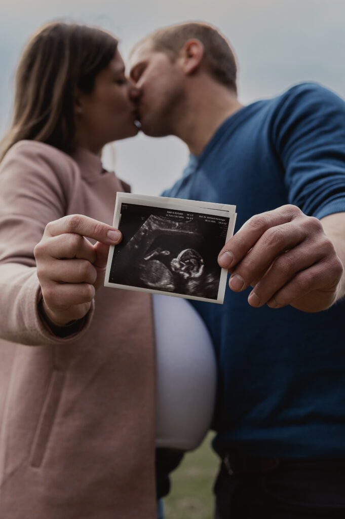 Babybauchshooting_Ybbs_an_der_Donau_Carografie_Caroline_Nagl-3966 Paar küsst sich und Streckt Ultraschallbild entgegen