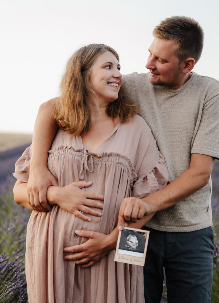 Fotoshooting_Lavendel_Carografie_Caroline_Nagl-101-Bearbeitet Werdende Eltern sehen sich an und halten ein Ultraschallbild in den Händen