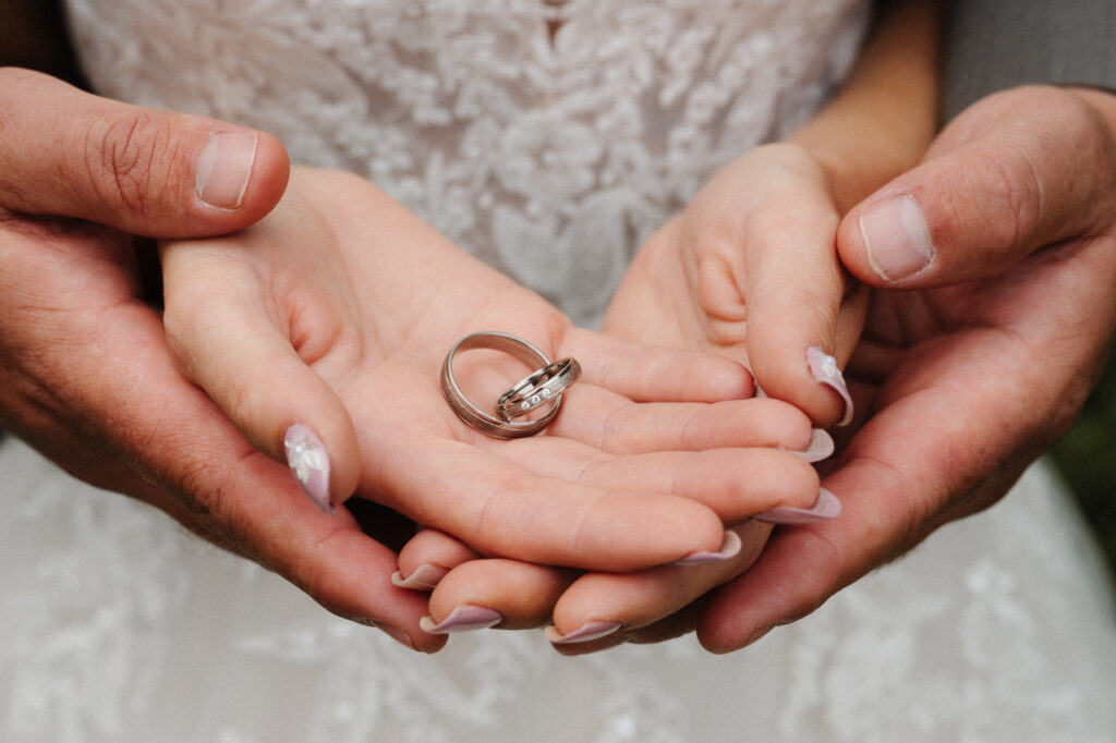 Hochzeitsringe in den Händen des Paares fotografiert