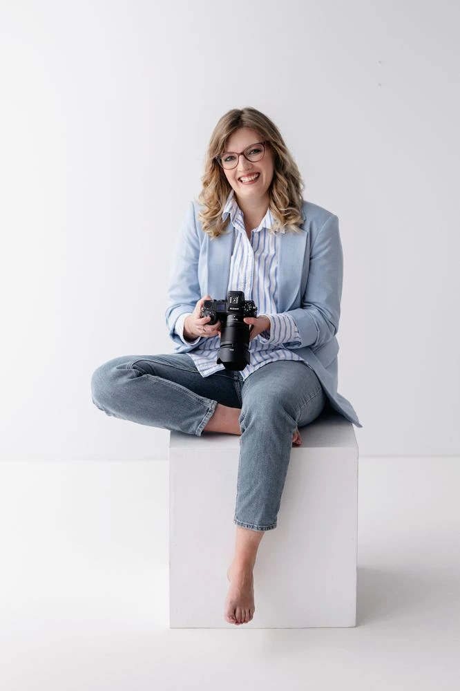 Die Fotografin Caroline sitzt mit der Kamera in der Hand auf einem Hocker.