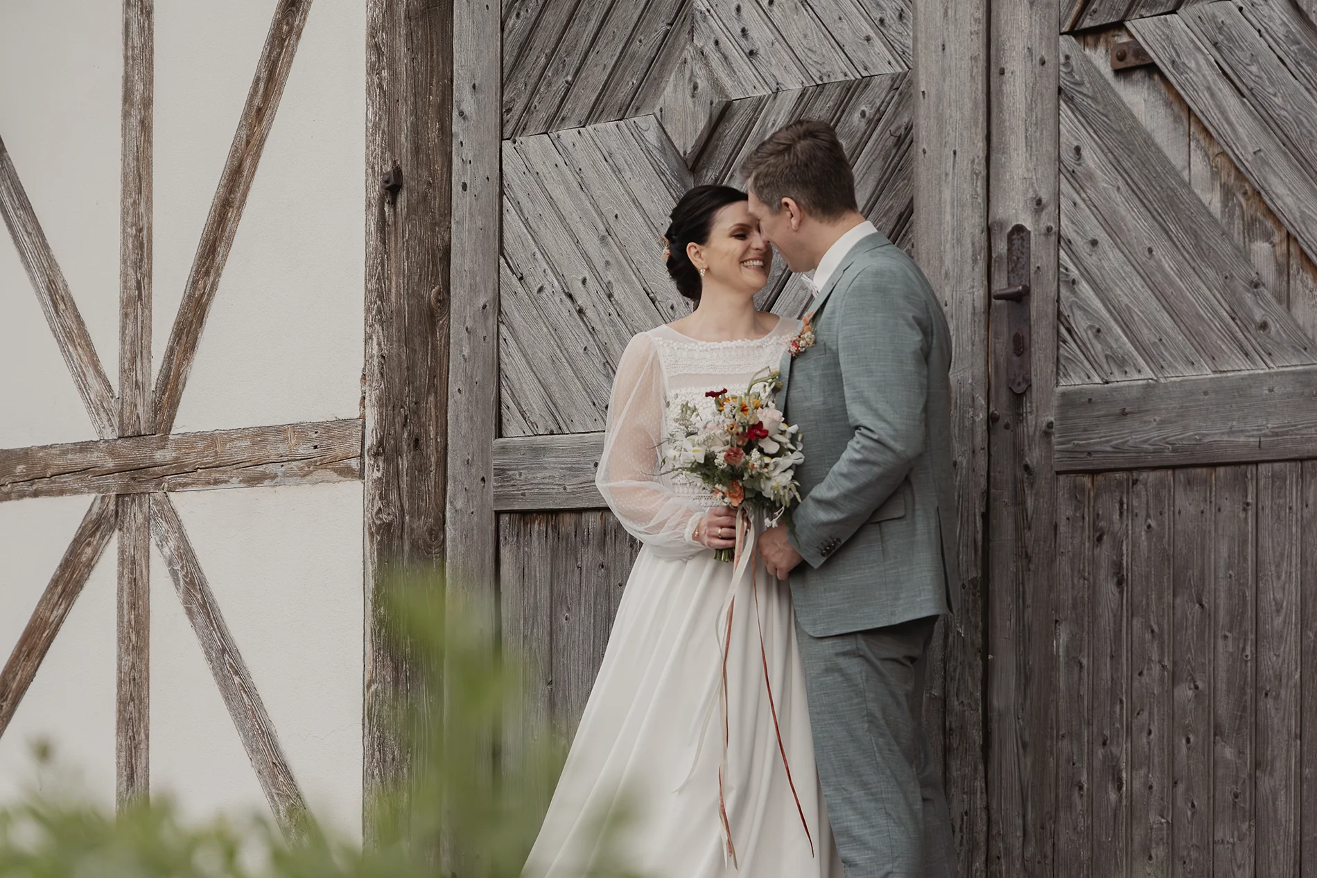 Hochzeitspaar posiert vor rustikaler Holztür