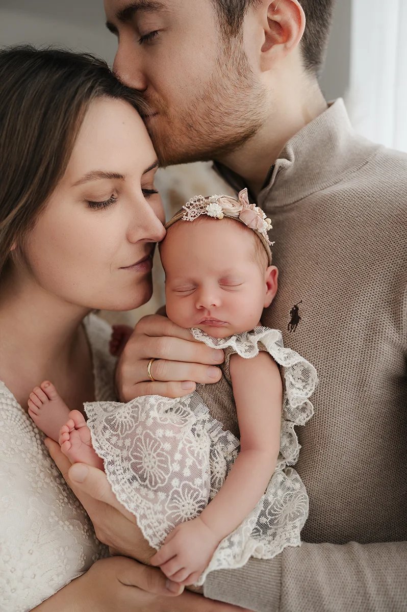 Mann küsst Frau auf Stirn während sie das gemeinsame Baby küsst
